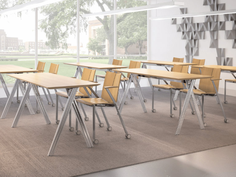 A classroom environment featuring six tables with natural wood tops. Each table has two chairs that are on casters.