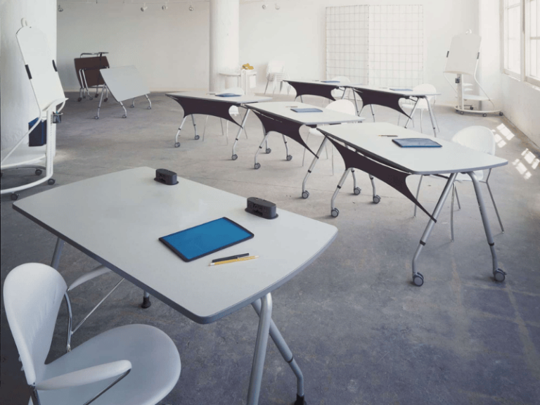 White, modern classroom with roll away tables and stackable chairs.